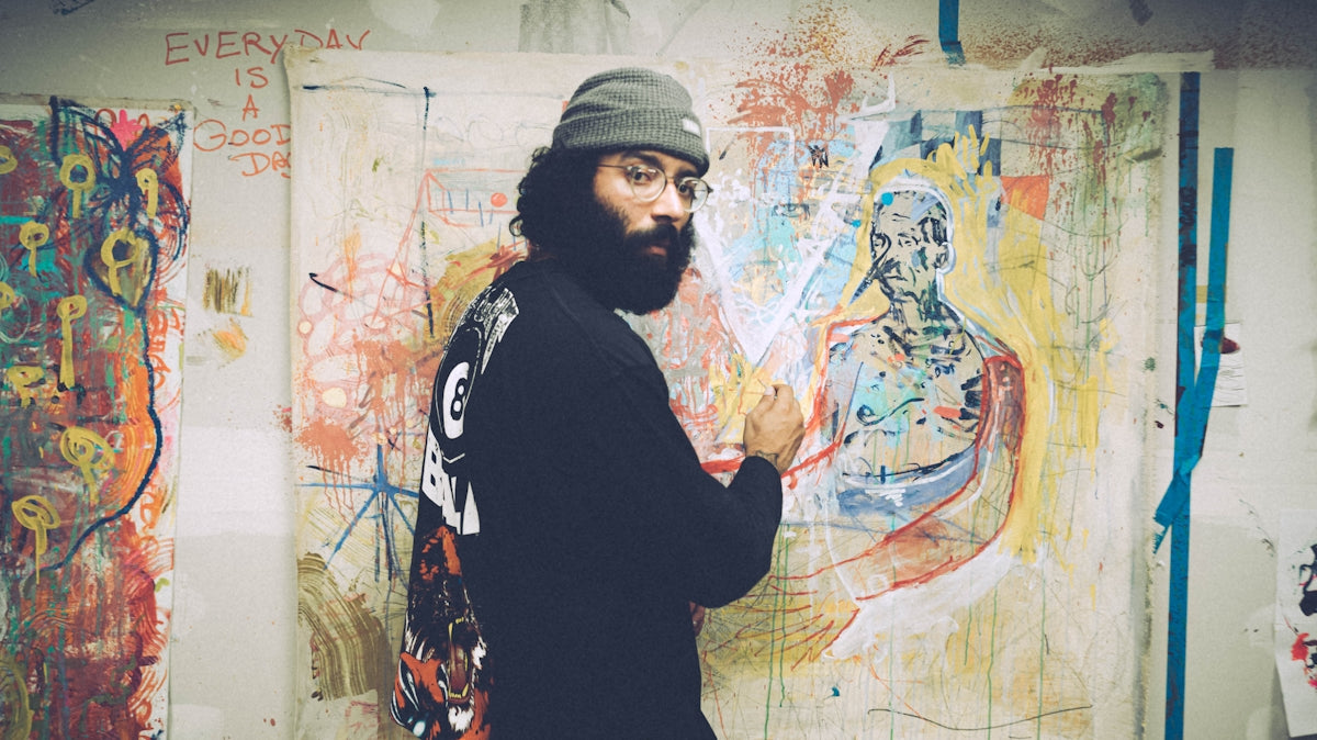 man in black and white sweater standing beside wall with graffiti