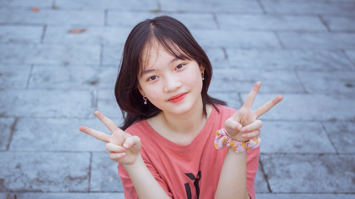 a young woman sitting on the ground making a peace sign