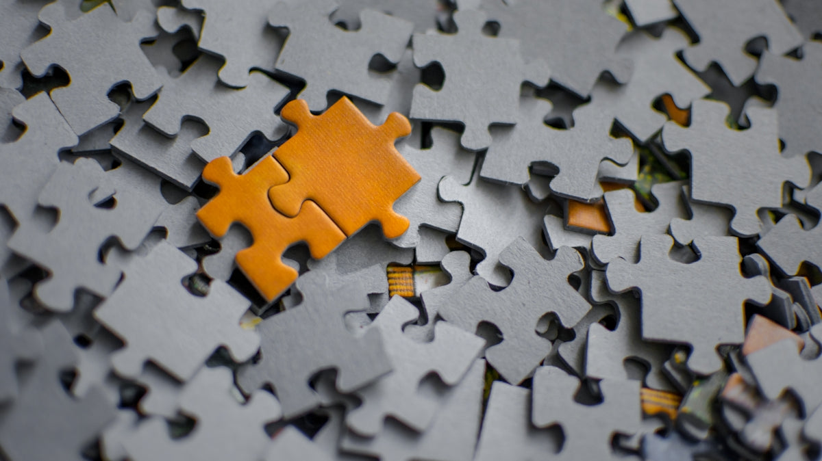 A single orange puzzle piece rests on a pile of grey pieces.