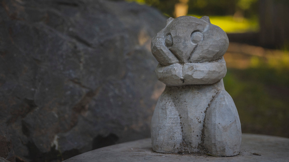 Wooden owl carving sits on a rock outdoors.